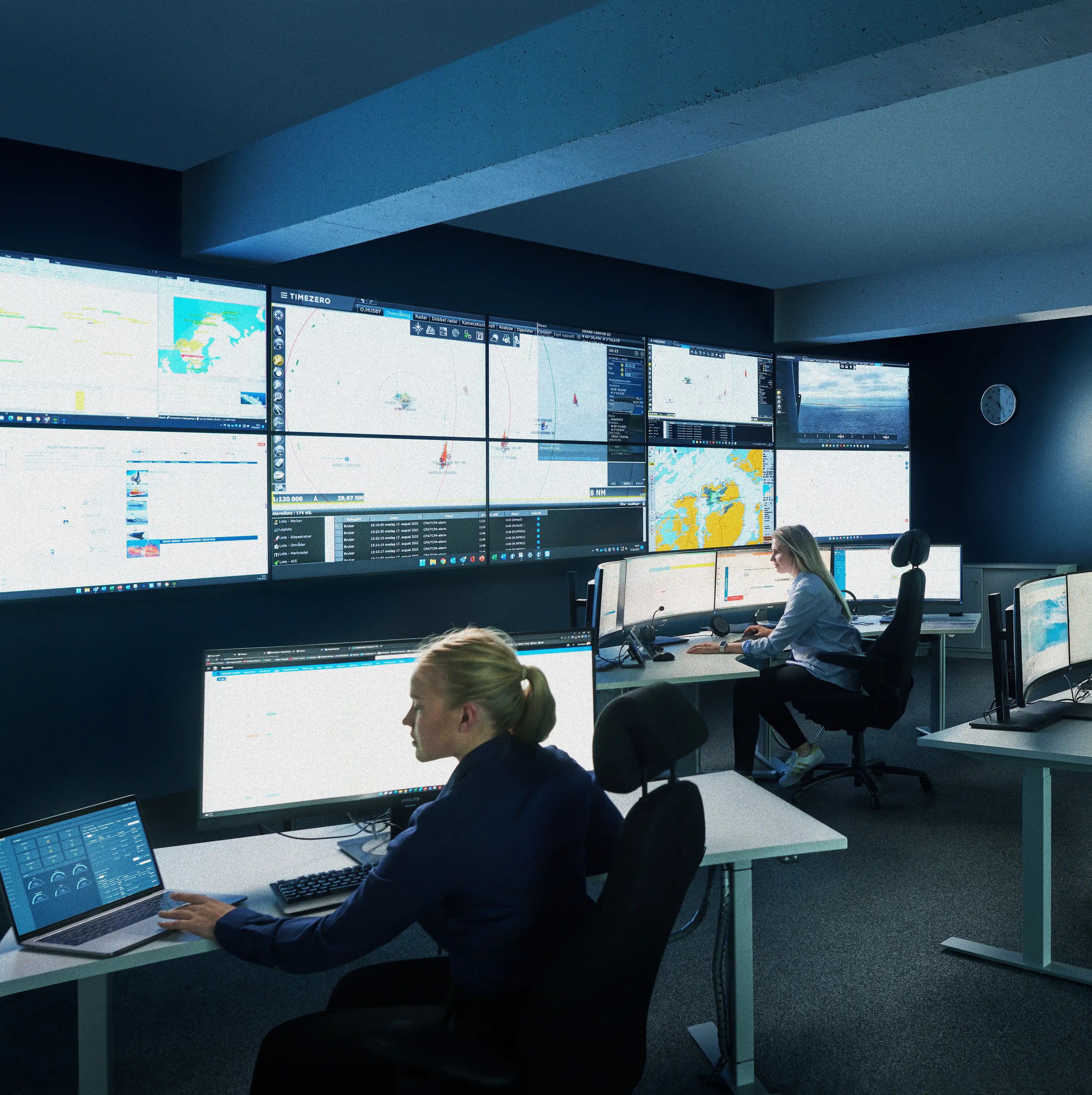 Bildet viser havovervåknings- og beredskapssentralen til Norseye. Veggen er dekt av skjermer som viser områdene som overvåkes. På sentralen sitter det to kvinnelige ansatte på hver sin pult og overvåker monitorene foran seg. 